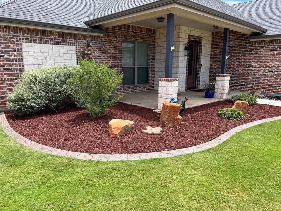 Finished curved red-mulch landscape bed bordered by green lawn